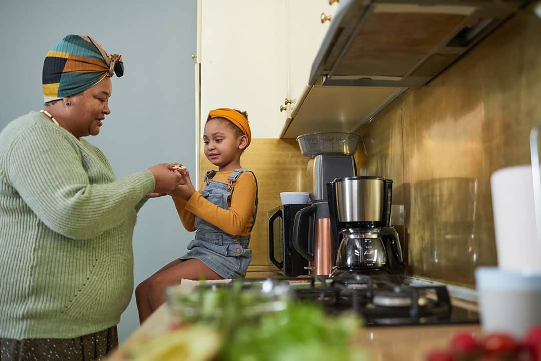 A grandmother with her granddaughter sharing a snack in their home kitchen.